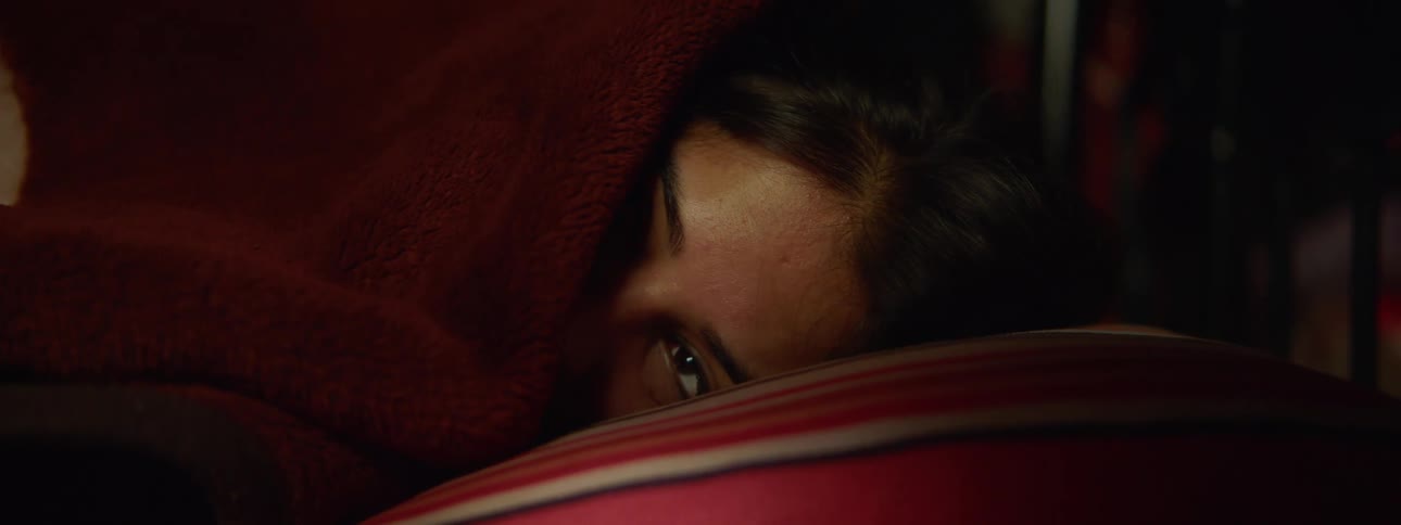 A woman lies in a bed with her face partially covered by her bed sheets