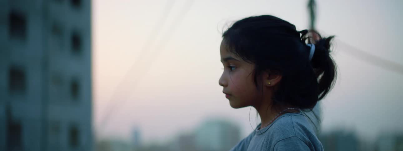 A little girl on a rooftop with buildings the sky and clouds in the background