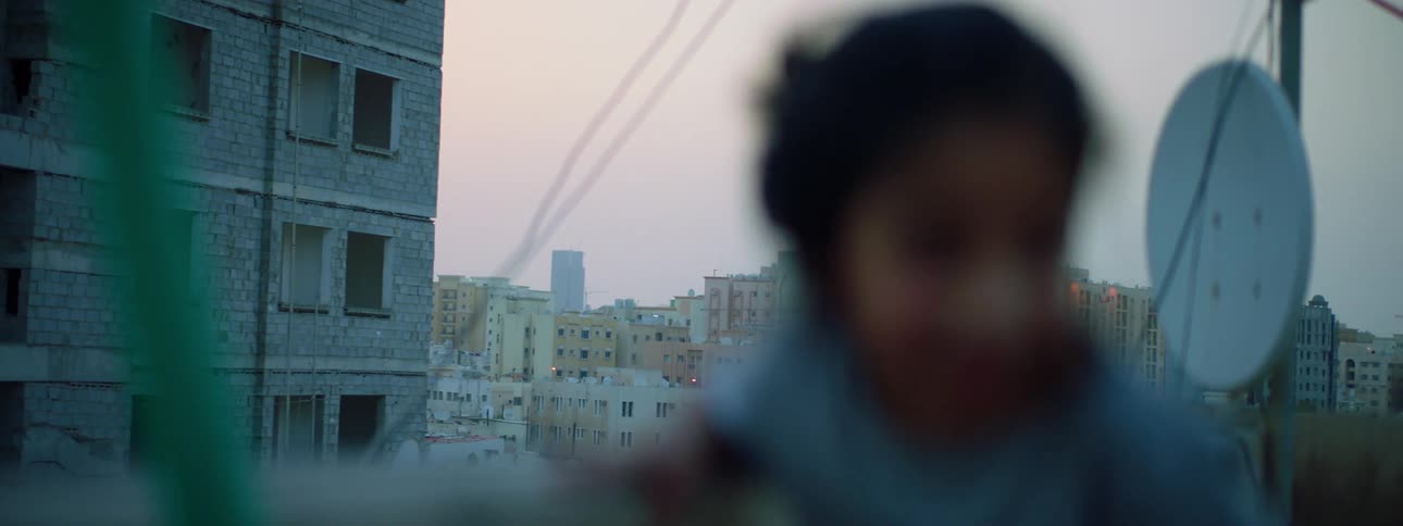 A young girl on the roof of a building looks out over the city before climbing down from her seat near the ledge