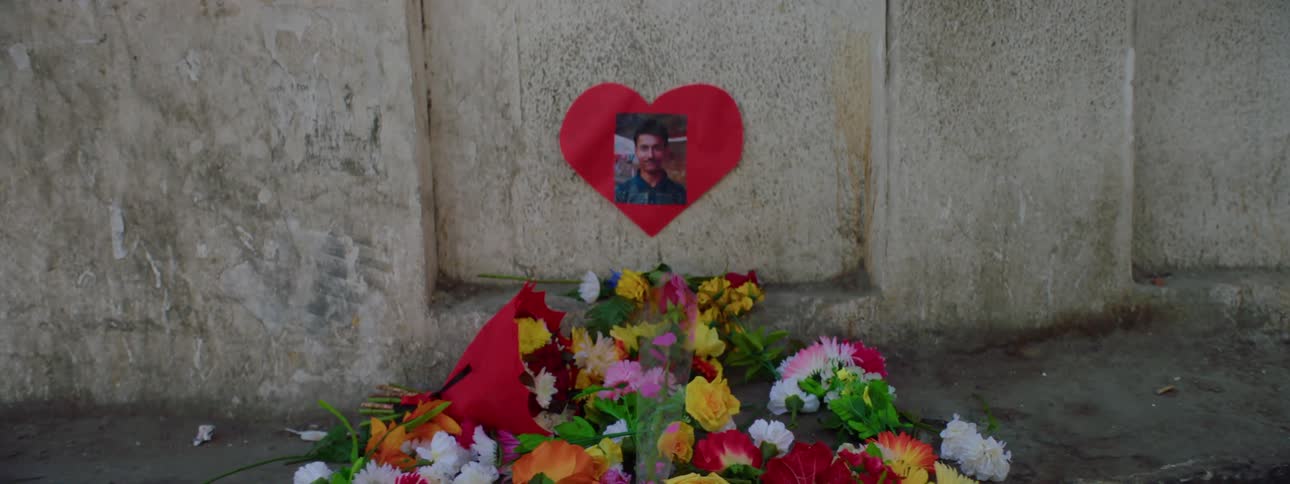 Woman walks past man setting flower to joins small memorial for man in picture