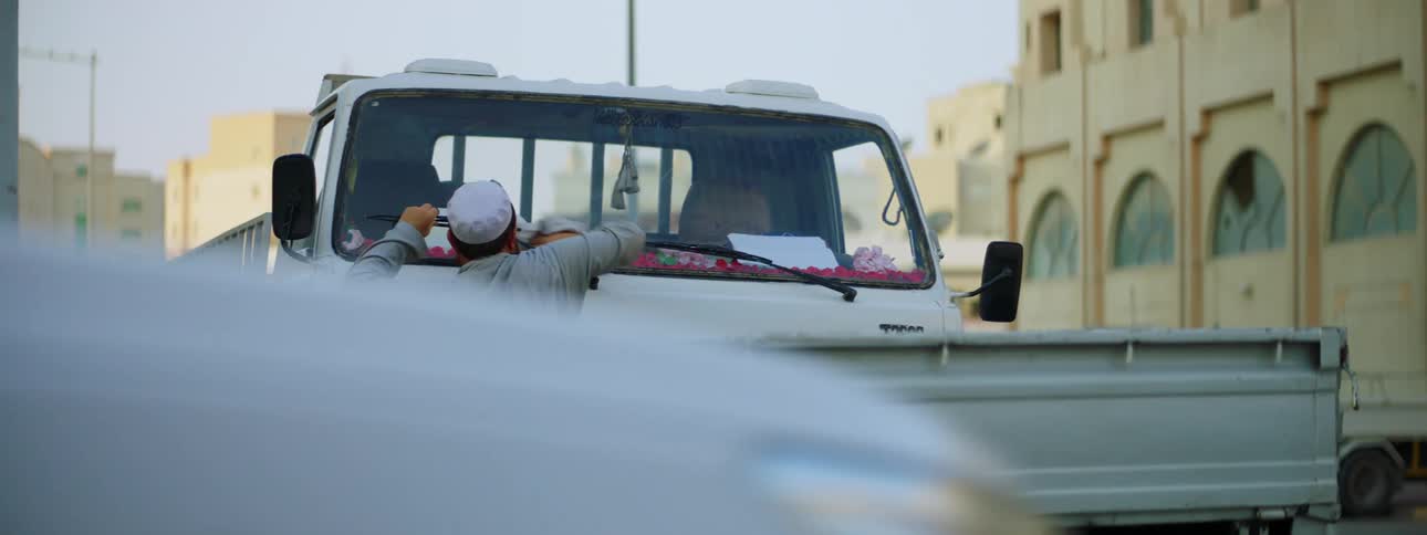A man washes the windshield of his truck with a cloth as pedestrians walk nearby