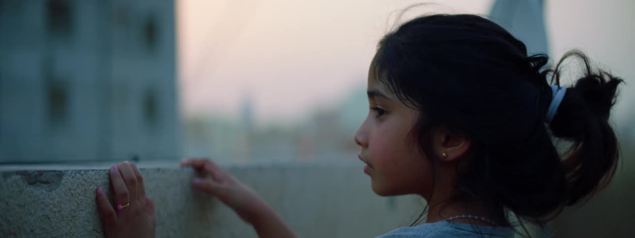 A little girl on a rooftop with buildings the sky and clouds in the background