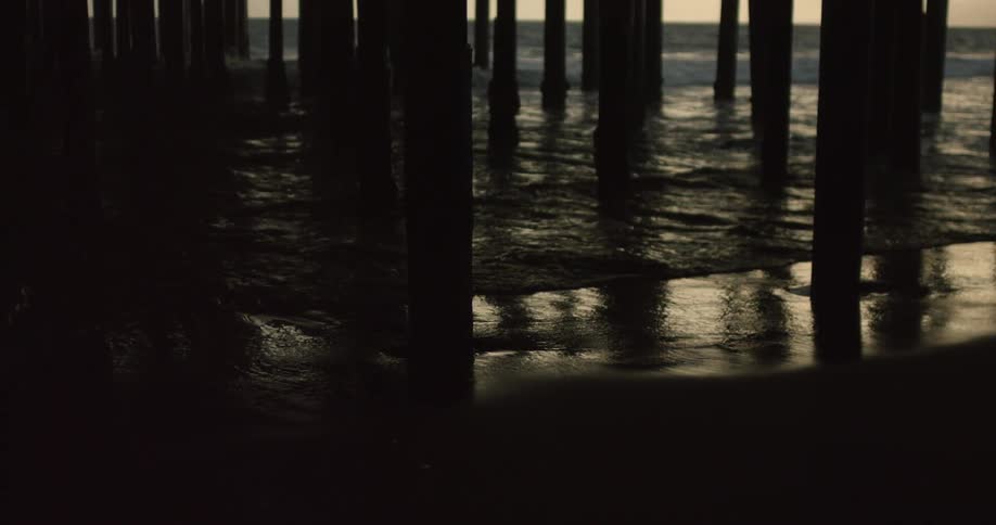 Ocean waves wash ashore beneath a pier