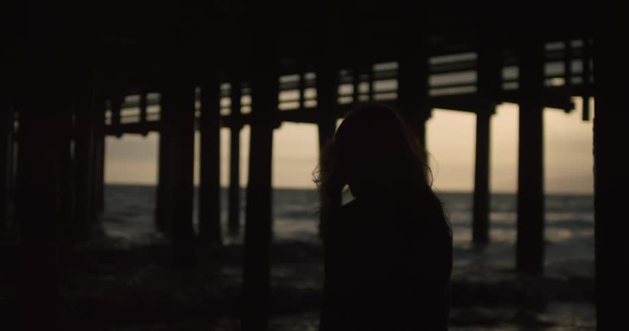 A woman walks beneath a pier at the beach at dusk