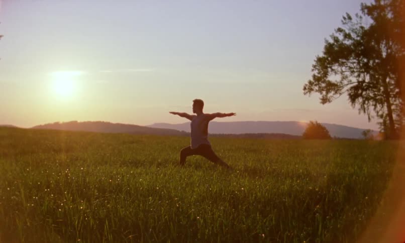 A man does yoga in a field of grass under a low sun