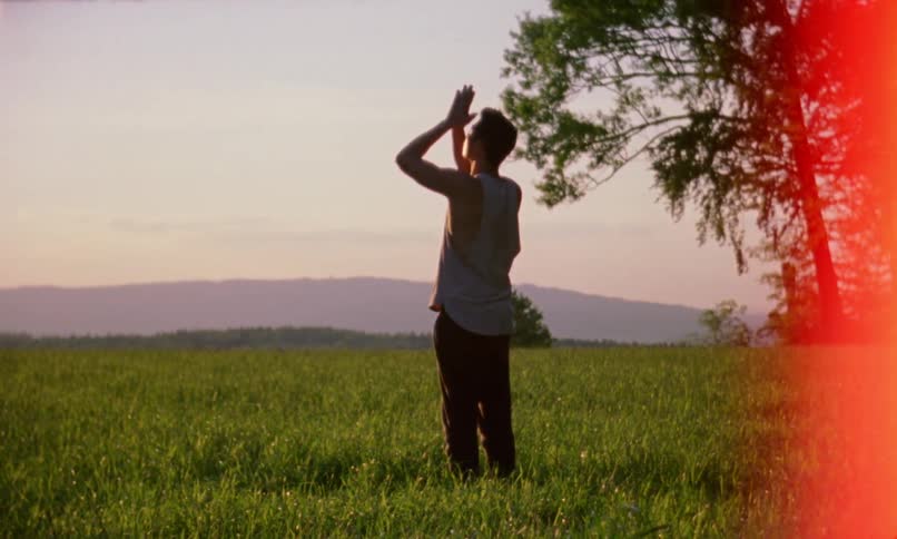 Man stands in a field and reaches up with his arms then brings them down as he stretches