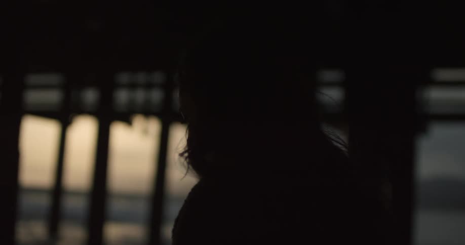 A long haired person walks under a bridge at sunset