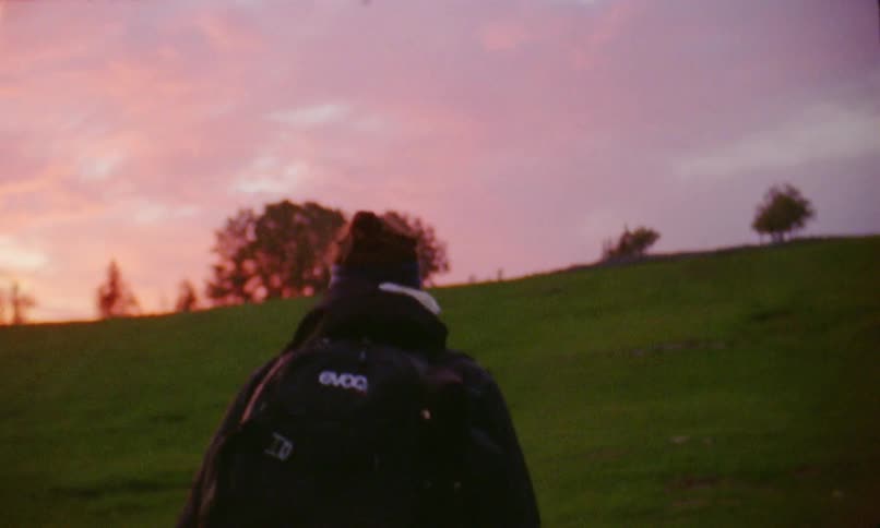Man with a headband and a black backpack walks uphill at sunset