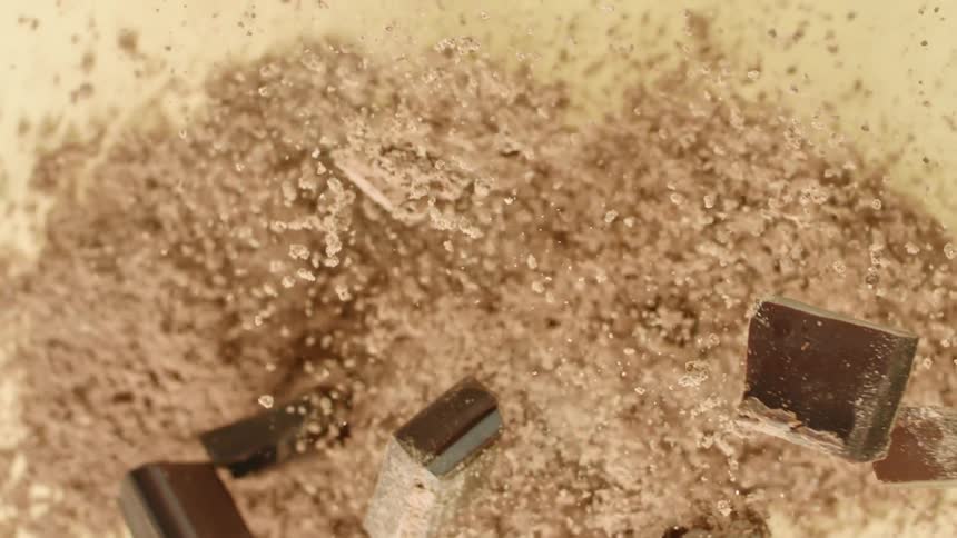 Dark chocolate chunks and grounded cocoa jumping on a surface in slow motion