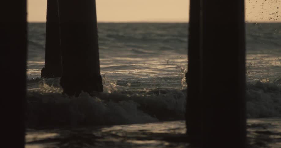 Waves are crashing on the shore under a pier