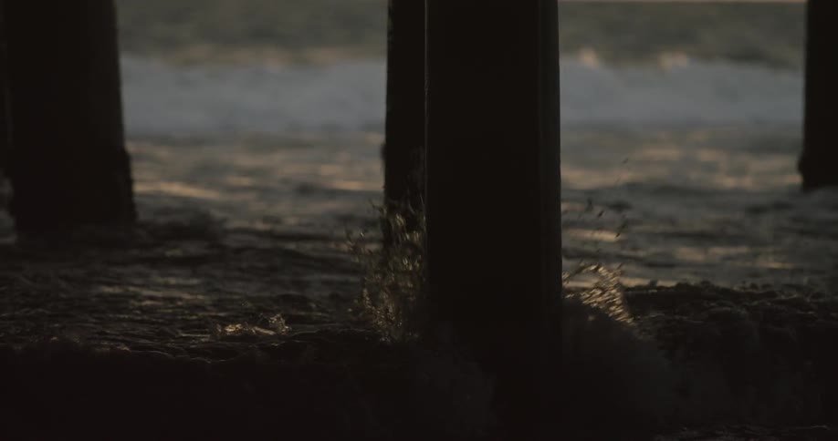 Ocean waves splash against the wooden legs of a pier