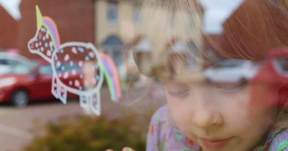 Young girl looks at a drawing on a window as cars sit parked on the street