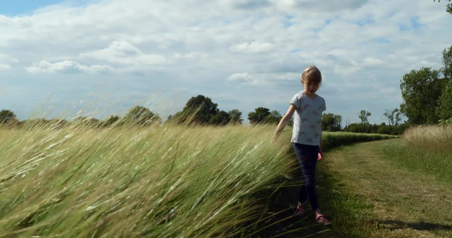 A girl and a boy with a helmet walking next to a grassy field with trees the sky and clouds in the background