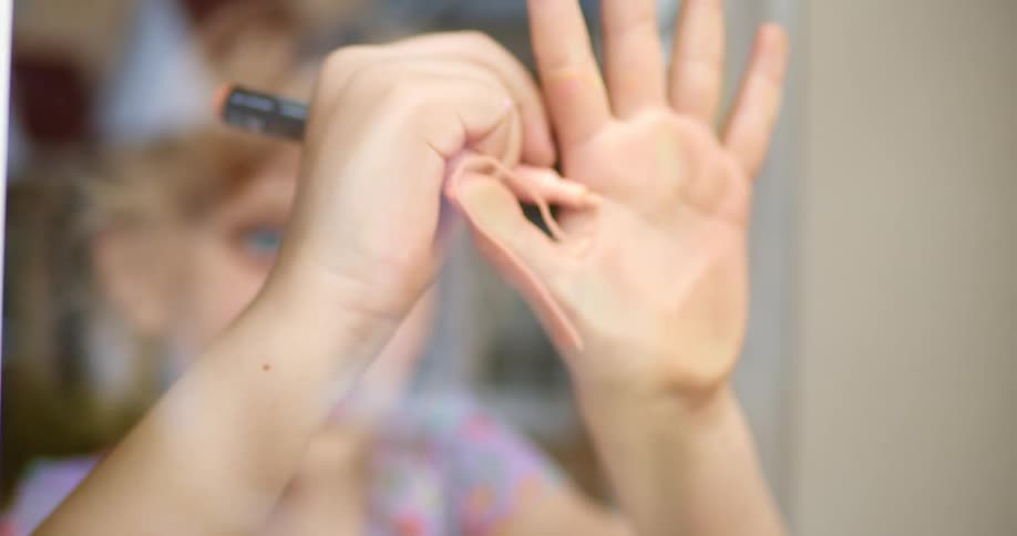 Female child smiles as she uses a peach marker to trace the outline of her hand on the inside of the window in her home