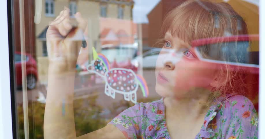 Young girl drawing on a window pane indoors