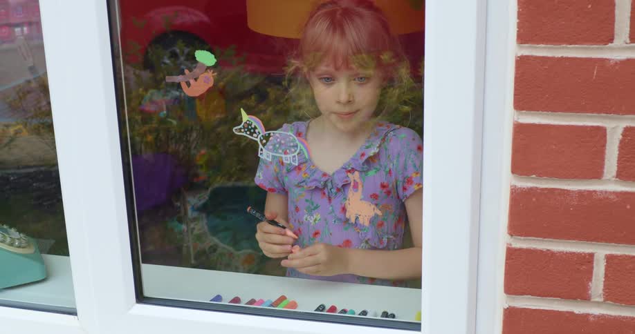A young girl uses markers to color on a home window