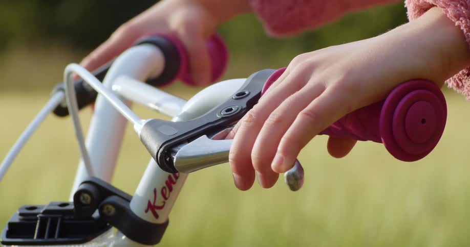 A person hands holding on to a bicycle handle and squeezing the brakes with grass and trees in the background