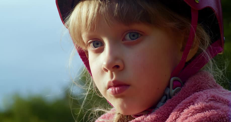 Blonde girl with a pink helmet and jacket looks at the camera