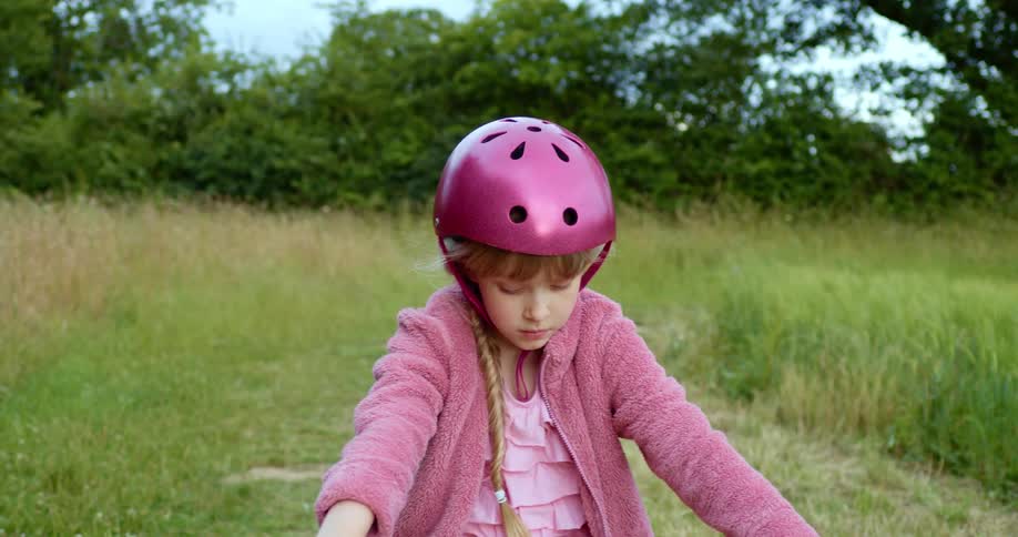 Blonde girl with a pink helmet and jacket sits on a bicycle seat in the countryside