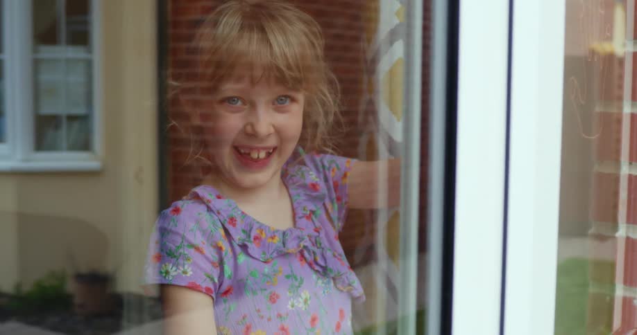 Little child with blonde hair smiles brightly behind windows in the room
