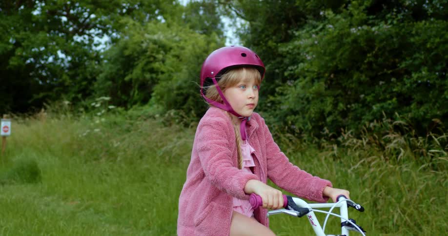 A little girls rides her bike past a wooded area