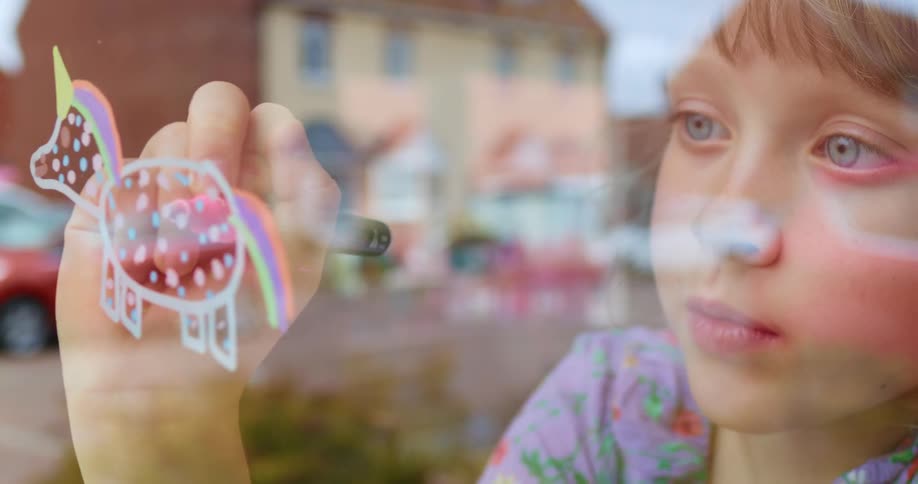 A little girl colors on the window of her house