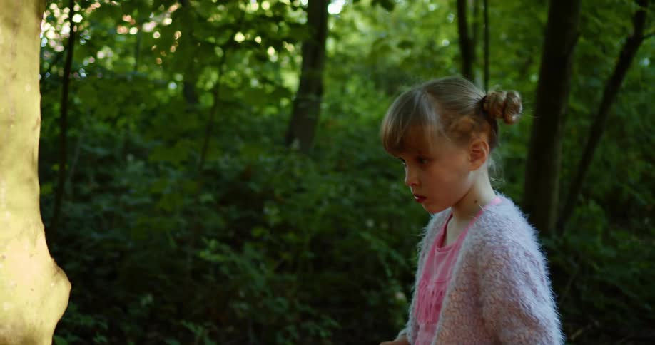 Young girl walks in the forest then turns to her left and looks up