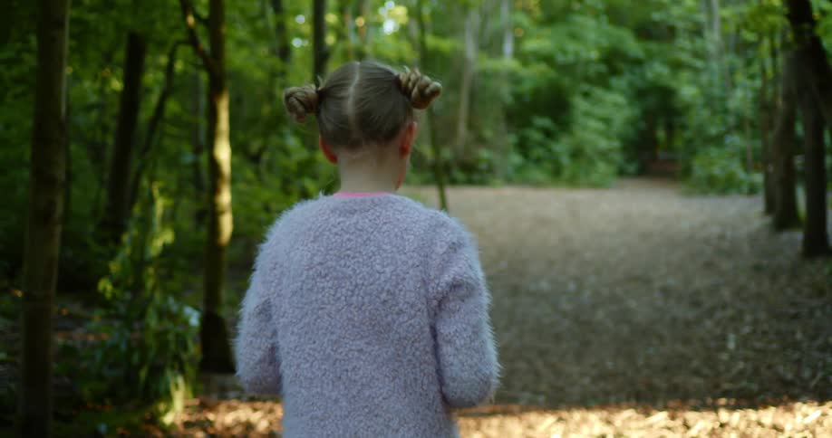 Blonde girl with a grey pullover walks on the brown leaves in the forest