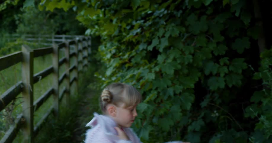 A little girl sitting on a fence jumps down and runs in to the trees