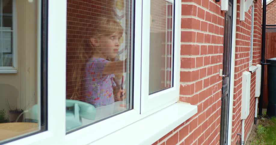 Girl inside a house draws on the window with a marker