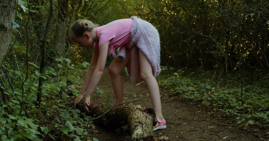 A young girl moves a tree trunk in a forest