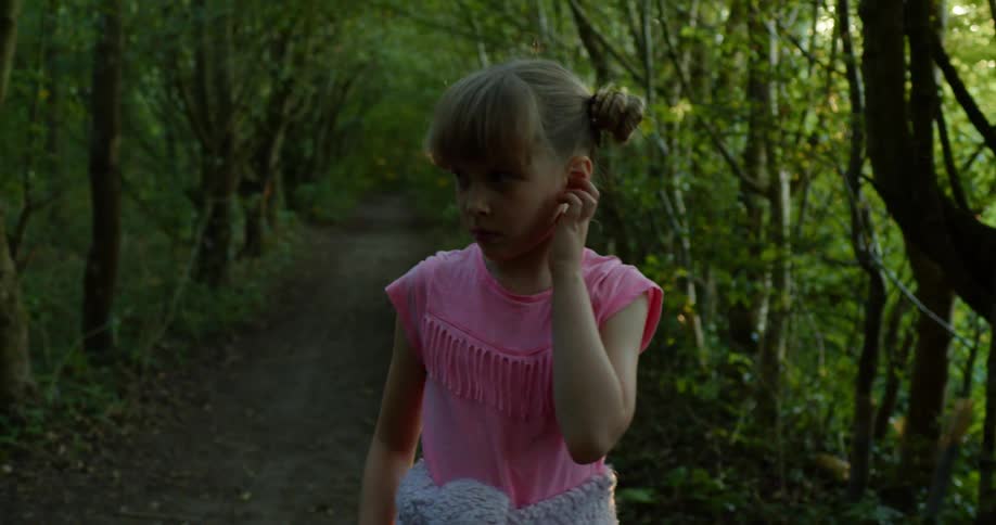 A young girl looks around as she walks in a forest