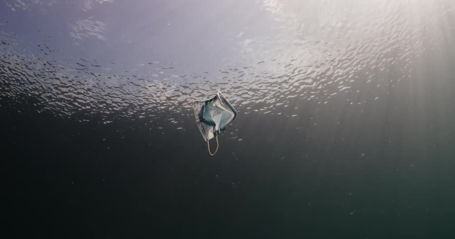 Sky shows through water surface as medical face mask floats beneath the water
