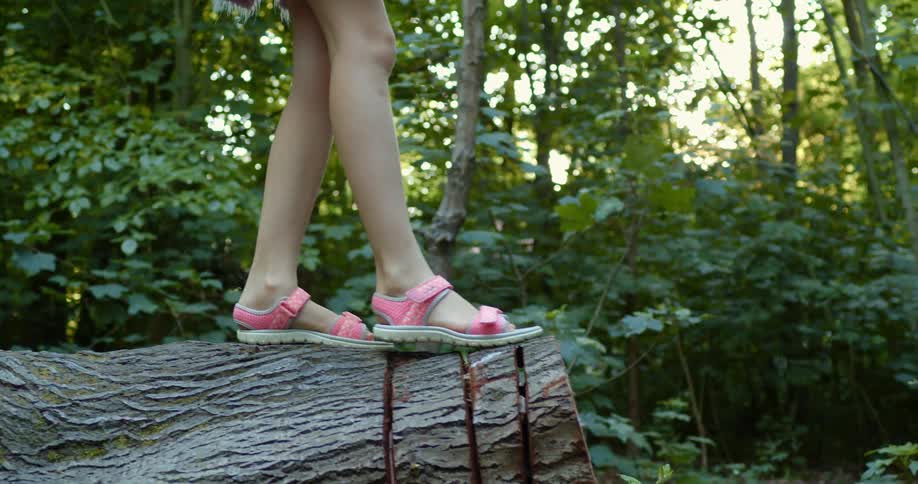 A young girl walks across a log in the forest and jumps down