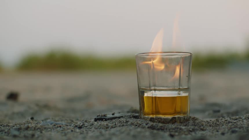 Flames burn in a glass of beer that is sitting on the ground