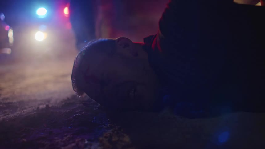 Blue and red lights from police cars flash as a man is pushed to the ground and arrested