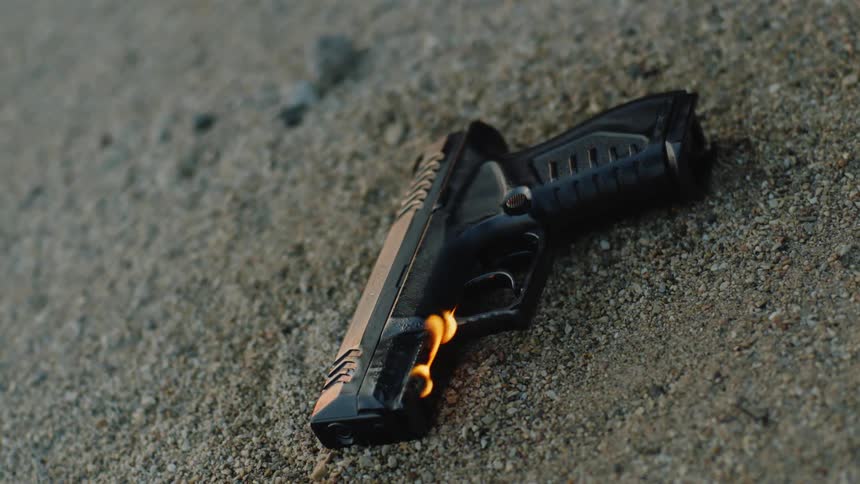 A gun laying on sand with fire and smoke on the front of the gun