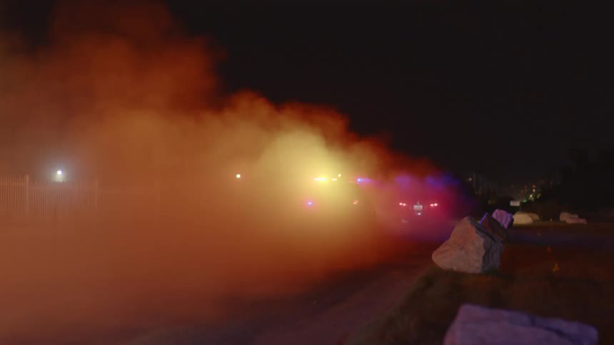A car being chased by police cars on the road at night with smoke and the sky in the background