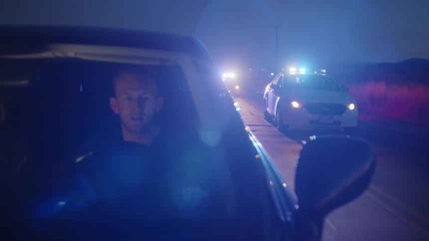 A man in a car being chased by the police with the sky and utility poles in the background