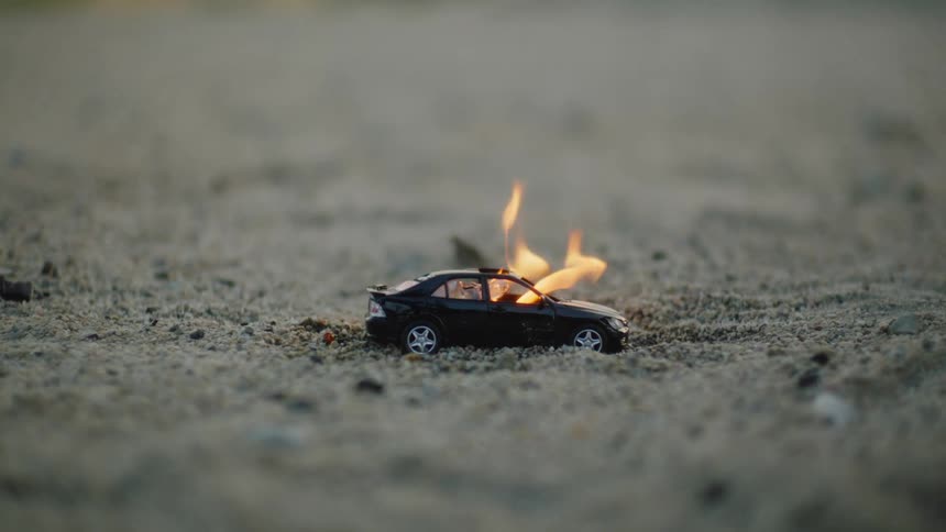 A toy car engulfed in flames on soil