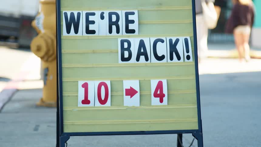 A sign on a sidewalk advertises that a store has reopened and its hours