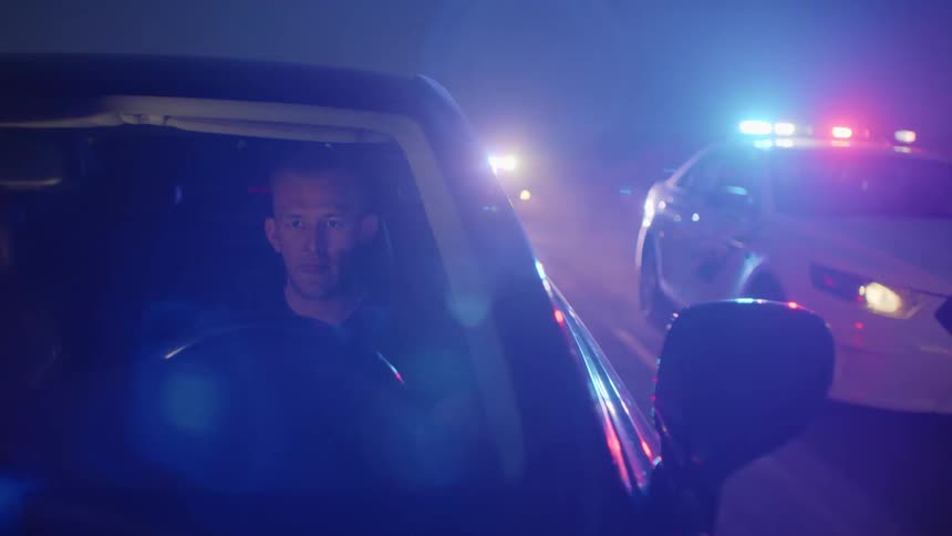 A driver is pursued by two police cars with lights flashing on a rural road
