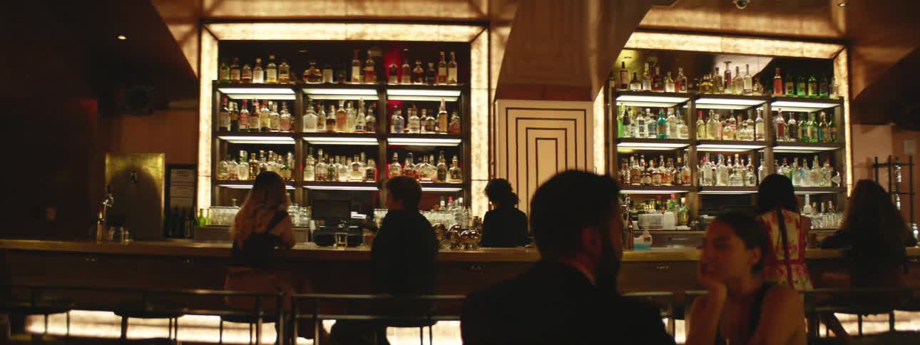 A man and a woman sitting at a table with a bar with people in the background