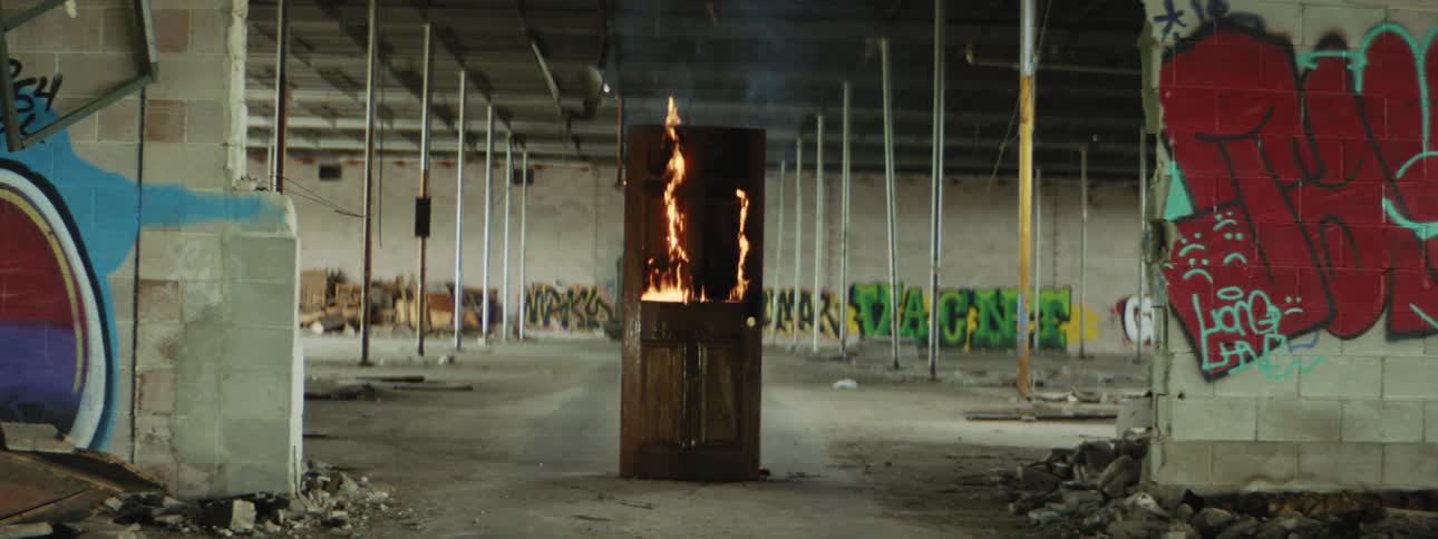 A fire burns a piece of furniture in a warehouse with graffiti