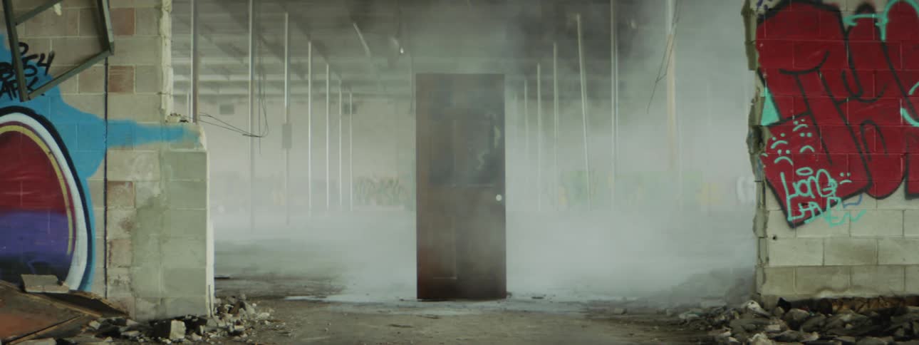 Smoke billows around a door standing in the middle of a warehouse