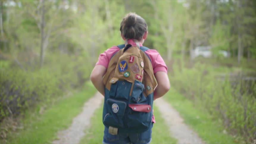 Girl with a pink shirt and backpack walks along a dirt road in the countryside
