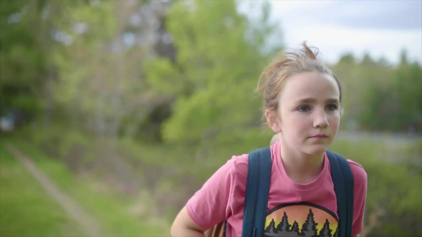 Blonde girl with a pink shirt and a backpack walks along a dirt road in the countryside
