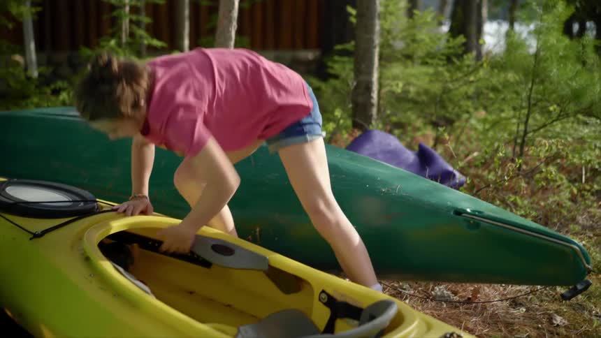 A girl tucks her backpack intokayak before beginning to pull the kayak towards the lake