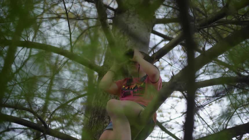 A girl is sitting up in the tree using binoculars