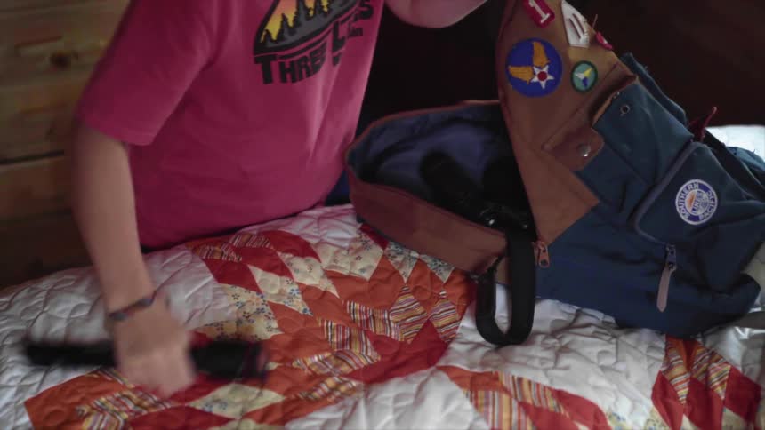A teenage girl puts a book camera and flashlight into her backpack